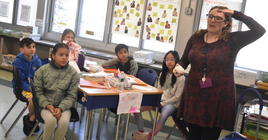 5 students at desk watching teacher